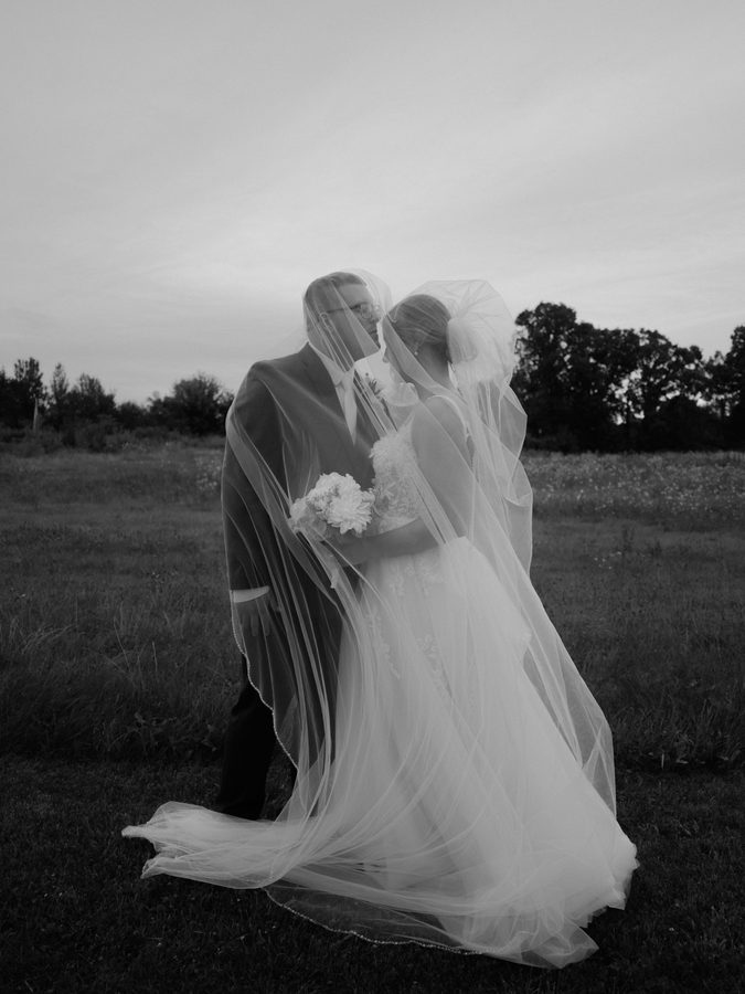 Alyssa and Eric under the veil in the field, black and white