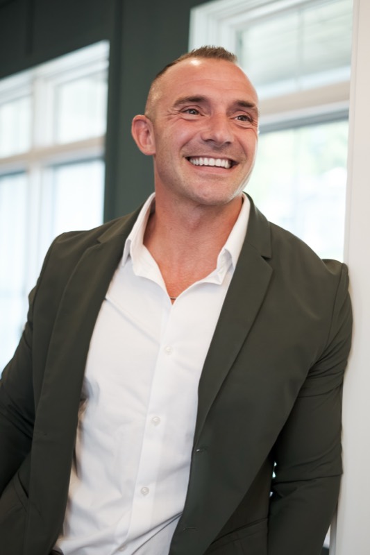 Scott Chain smiling, leaning in a doorway in a green blazer